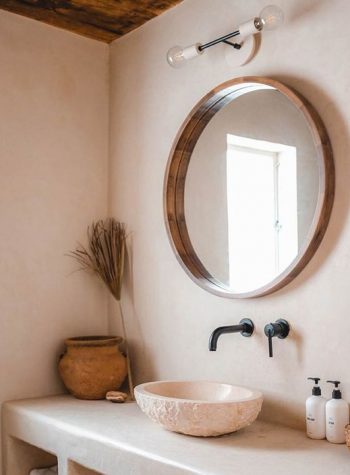 Earthen vessel sink set below a round wooden mirror with black matte faucet and fixtures