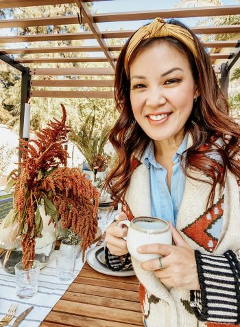 Anita wears a chunky, knit sweater holding a mug, standing in front of her completed tablescape
