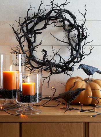 a black wreath of gnarled branches set above orange candles and a pumpkin staged with crow statues