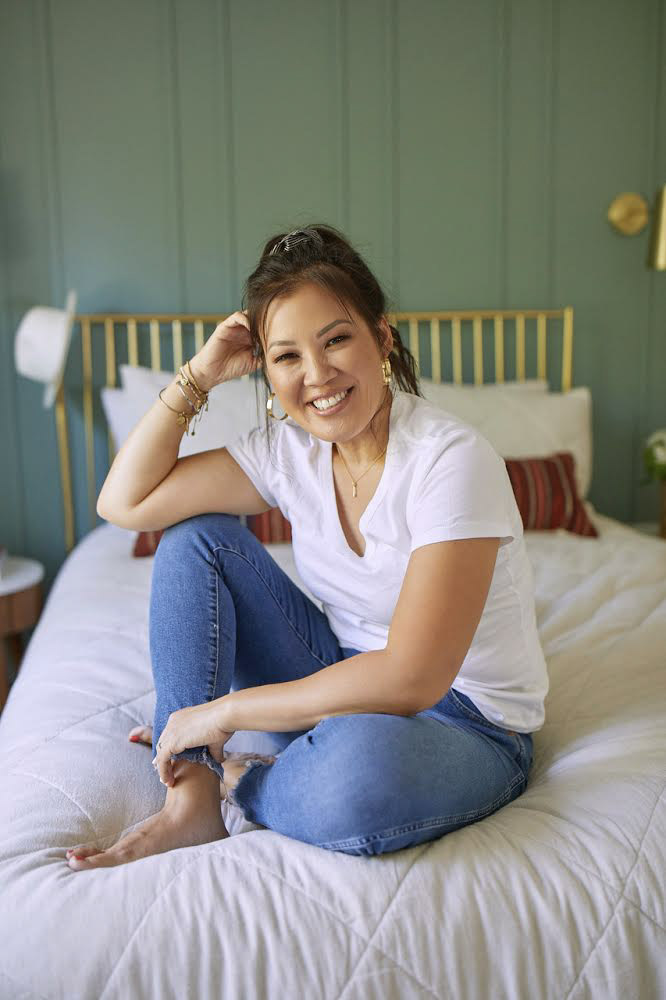 Anita sits on her bed in an easy white tee & jeans